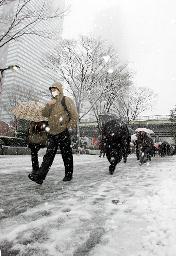 雪の降りしきるなか、足元を確かめながら職場などへ向かう人たち